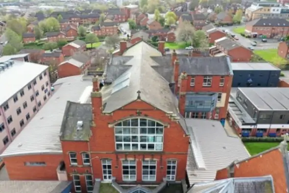 Aerial view of a red-brick building amid residential houses and green spaces.